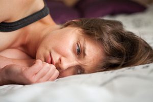 Image of young woman lying on bed looking worried and sad.