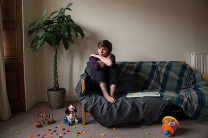 Image of young woman with toys scattered around her looking out window.
