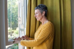 Photograph of woman looking out window feeling trapped.